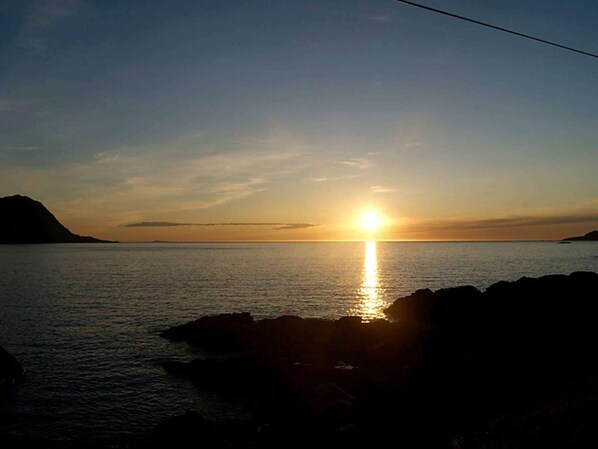 A sunset over a calm sea with rocky coastline. - Holiday Home in Gursken (Sande)