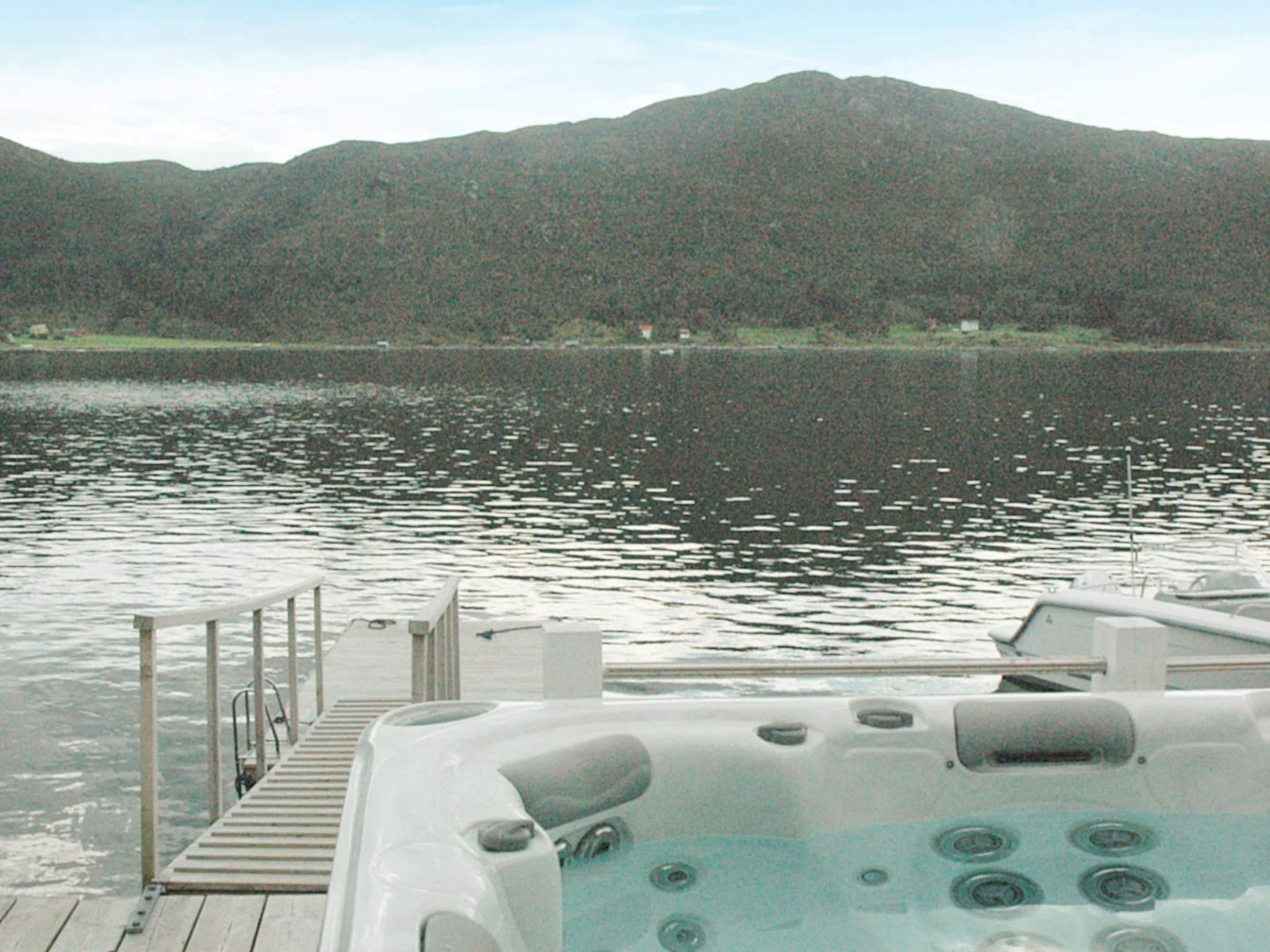 A hot tub on a wooden deck by a lake with mountains in the background.