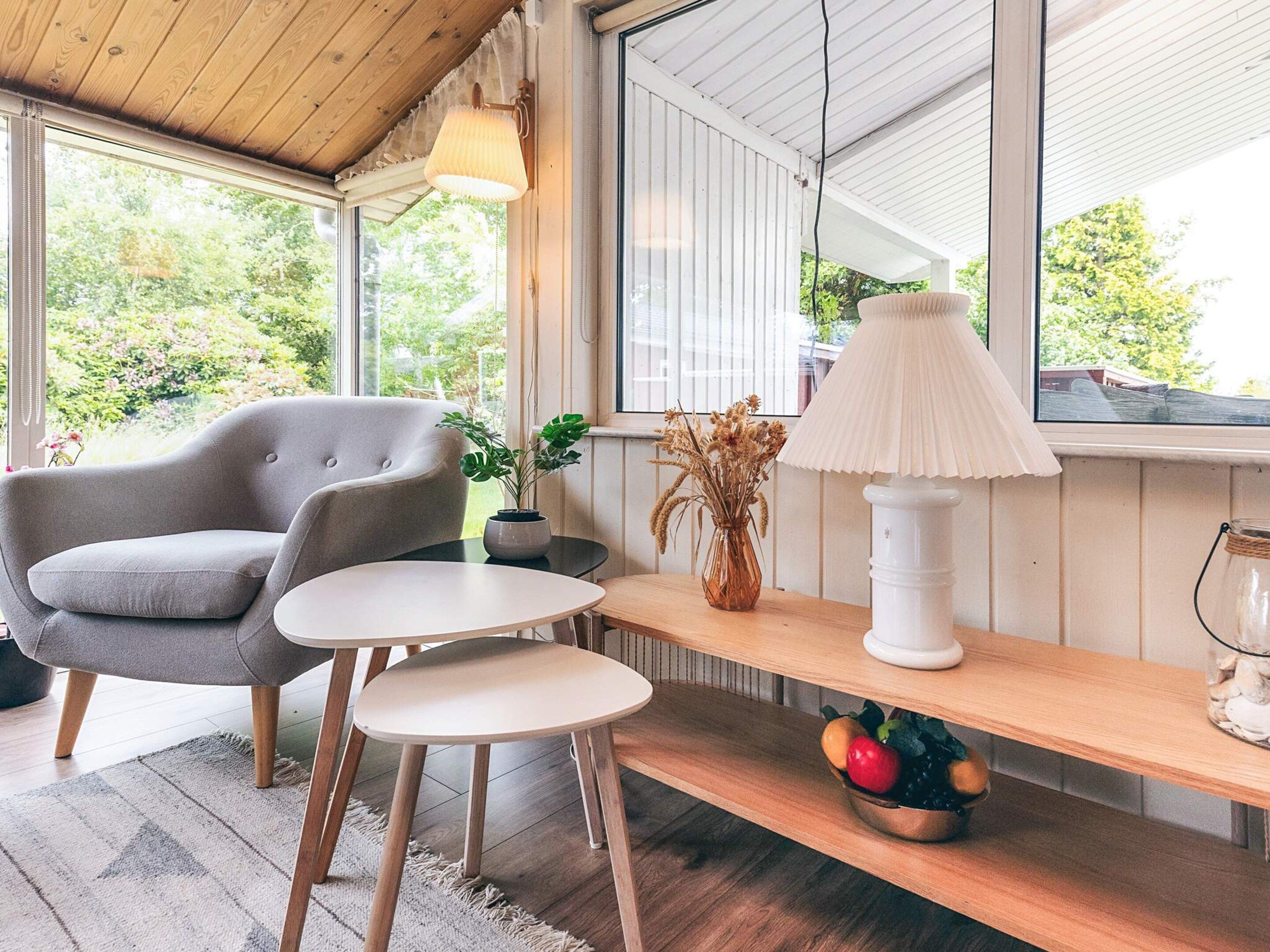 Een gezellige kamer met een grijze bank, een klein rond tafeltje, een lamp en een plankje met een schaal fruit.