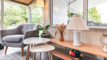 Een gezellige kamer met een grijze bank, een klein rond tafeltje, een lamp en een plankje met een schaal fruit.