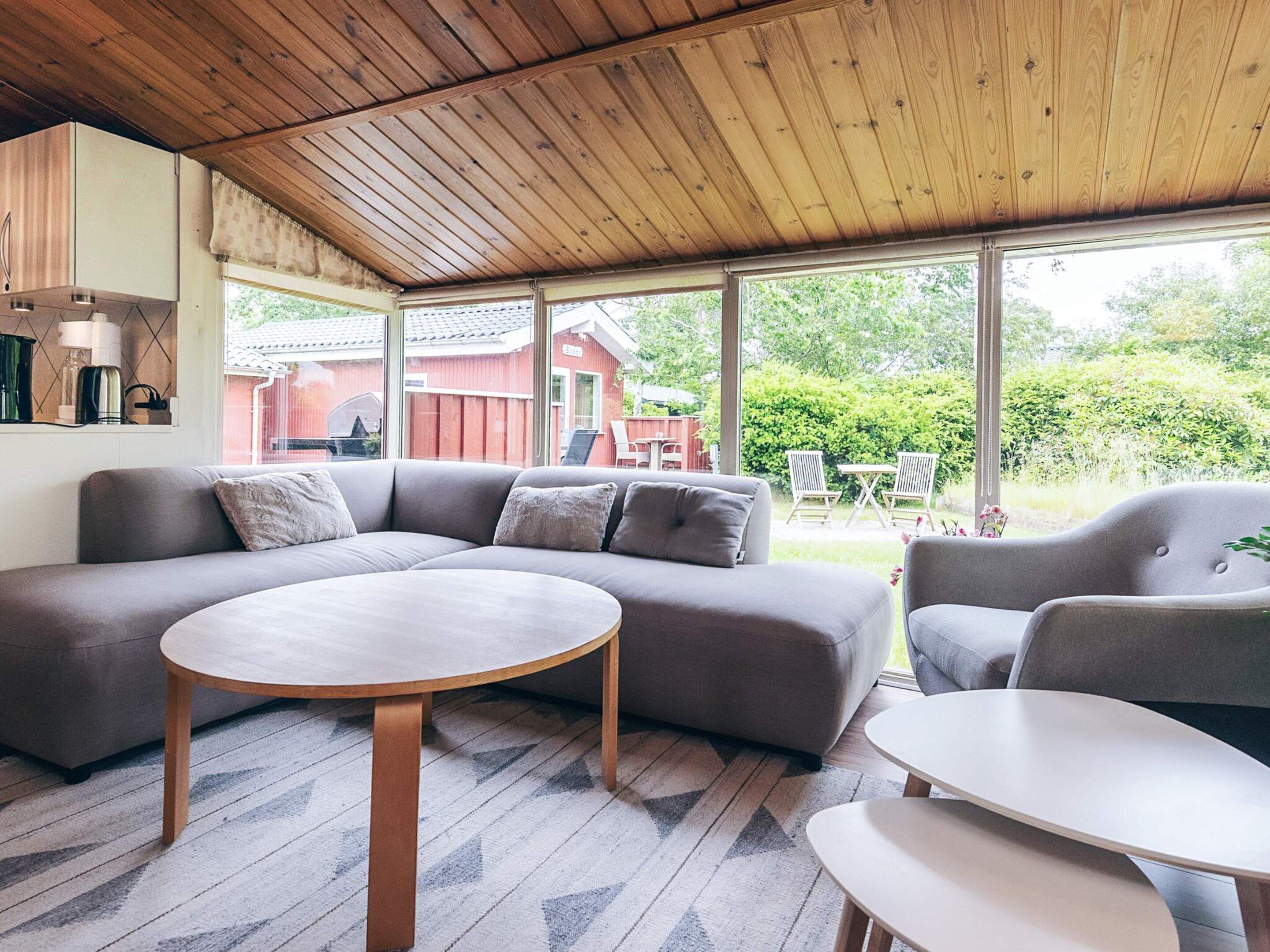 A modern living room with a sectional sofa, two armchairs, a round coffee table, and a dining table. Large windows provide a view of the outdoors.