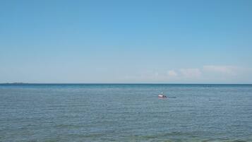 Een strand met helder water, een eiland in de verte en iemand die zwemt.