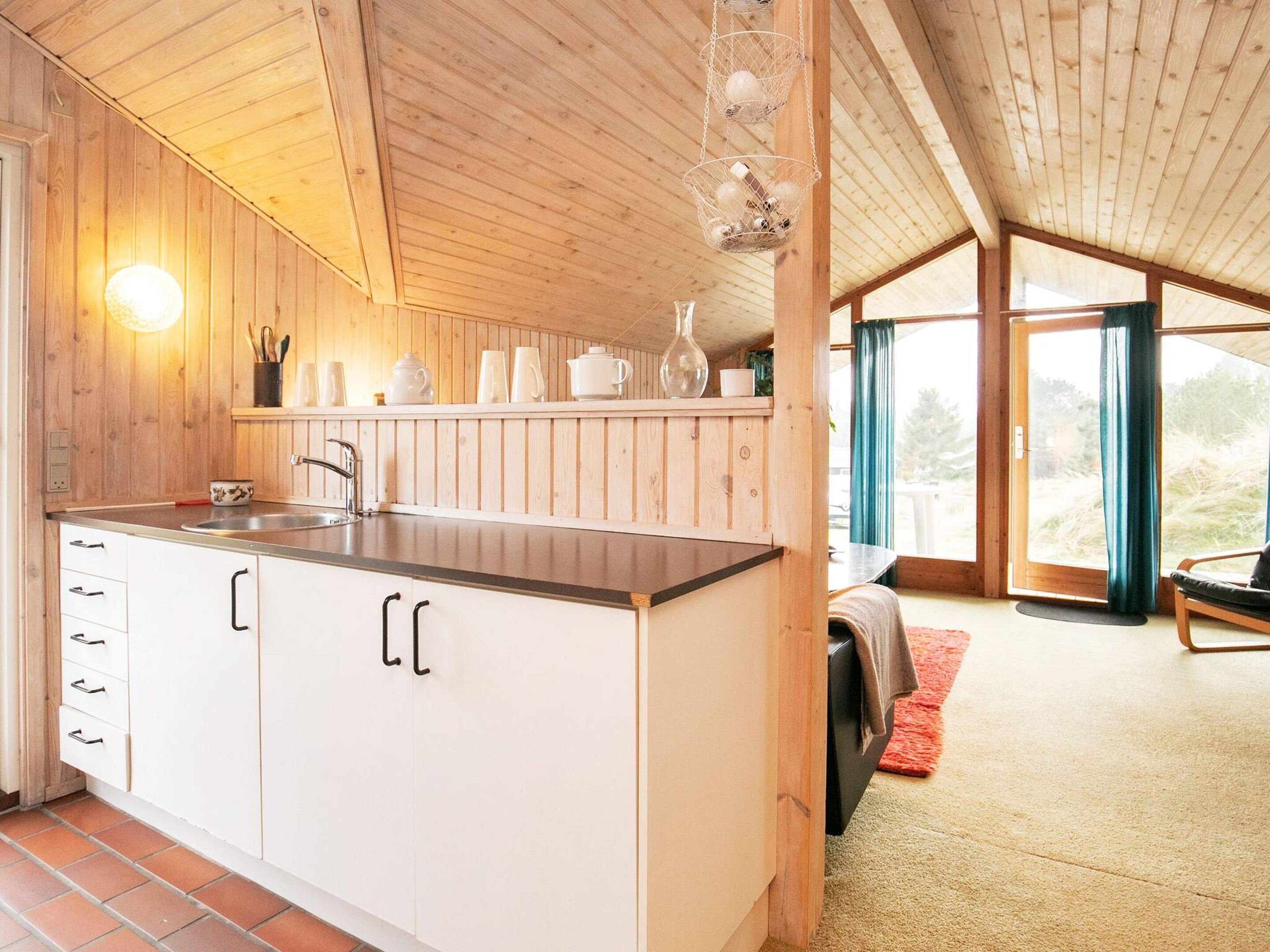 A kitchen with wooden cabinets, a sink, and a countertop. There is a window with a view of the outdoors.