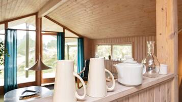 Interior de madera con una larga barra que muestra tazas blancas, un calentador de agua y un florero de vidrio.