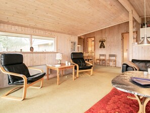 A room with wooden walls and ceiling, a red carpet, two black leather chairs, a small wooden table with a lamp, and a round table with a red rug. - 4 Person Holiday Home in Blokhus (Blokhus)