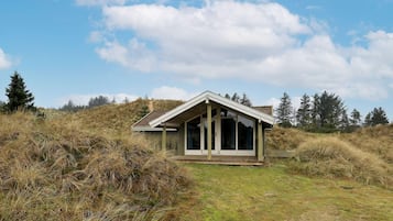 Uma casa moderna com telhado inclinado e amplas janelas, inserida em paisagem natural e cercada por árvores.