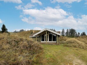 Una casa moderna con techo inclinado y amplios ventanales, rodeada de paisaje natural y árboles.