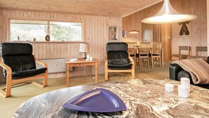 A cozy room with wooden walls and ceiling, a dining table with chairs, a sofa, and a purple table centerpiece. - 4 Person Holiday Home in Blokhus (Blokhus)