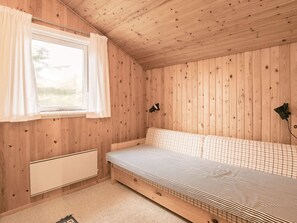 A wooden cabin room with a bed, a window with curtains, and a wall-mounted light fixture. - 4 Person Holiday Home in Blokhus (Blokhus)
