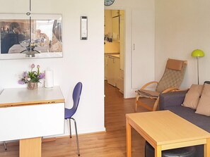 A compact living space with a dining table, a blue chair, a sofa, a lamp, and a kitchen area visible through an open door. - 4 Person Holiday Home in Nexo (Nexø)
