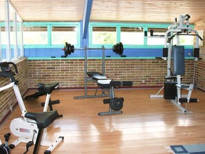 Een fitnessruimte met trainingsapparatuur, een bakstenen muur en ramen.