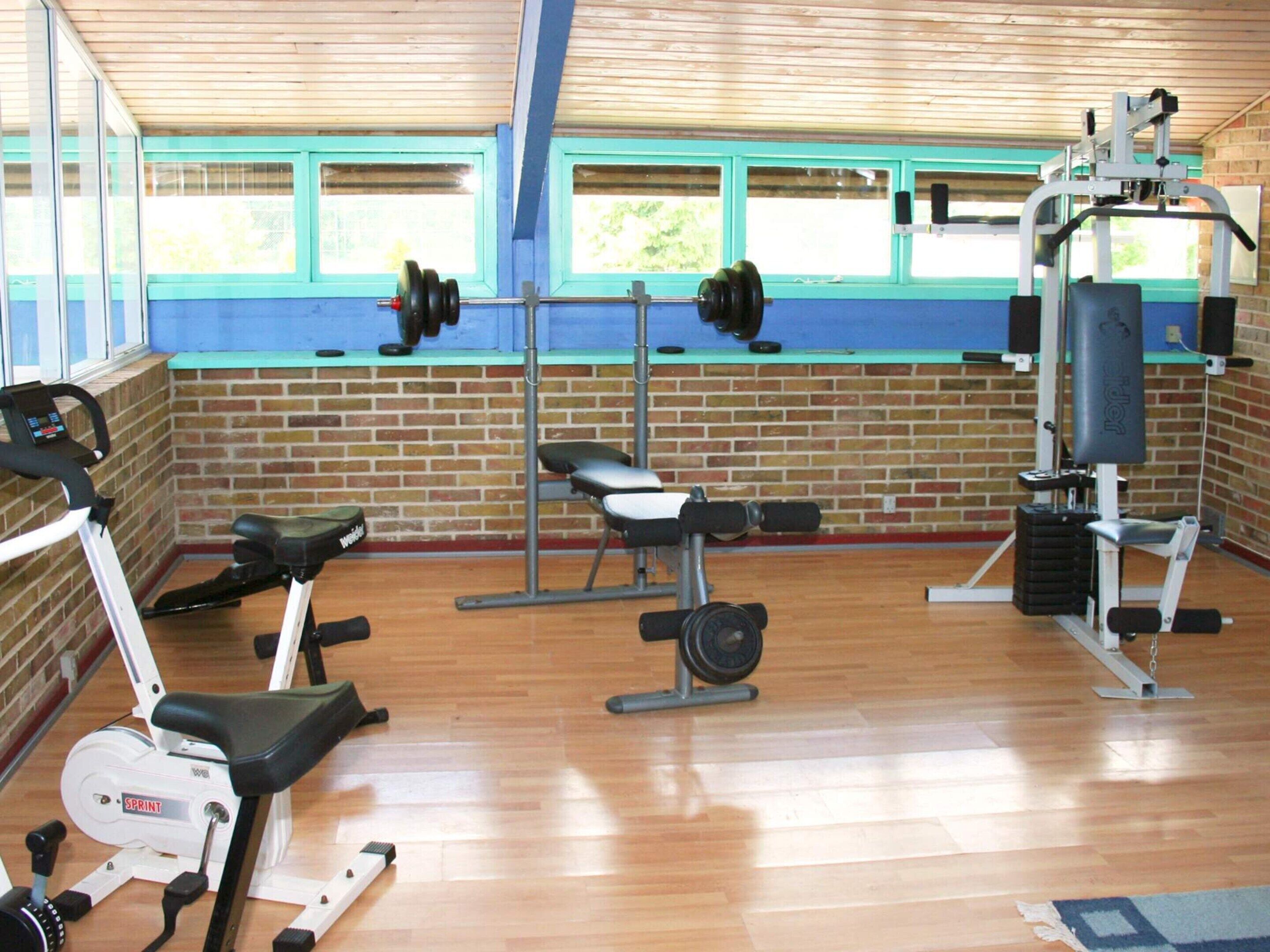 Un gimnasio con equipo de ejercicio, una pared de ladrillo y ventanas.