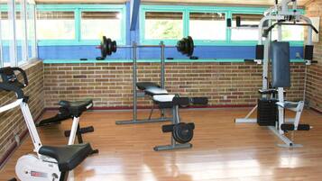 Un gimnasio con equipo de ejercicio, una pared de ladrillo y ventanas.