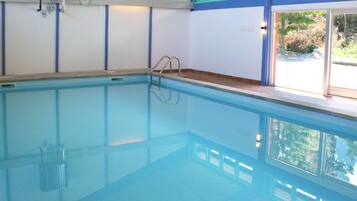 An indoor swimming pool with a clear view of the surrounding area, including a window with a view of trees and a door.