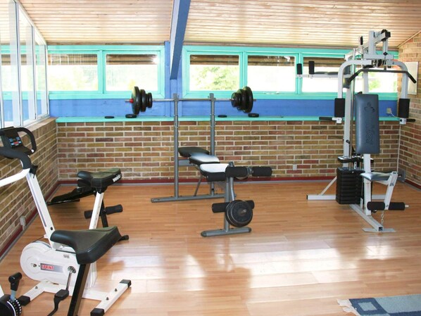 Une salle de sport équipée de matériel d’exercice, avec un mur en briques et des fenêtres.
