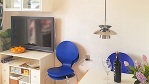 Une pièce avec une télévision, un fauteuil bleu, une bouteille de vin et un vase rempli de fleurs.