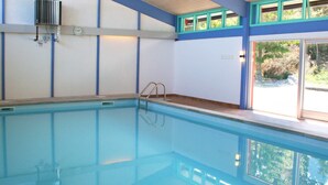 Une piscine intérieure offrant une vue dégagée sur l’extérieur grâce à de grandes fenêtres.