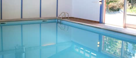 An indoor swimming pool with a clear view of the outside through large windows.