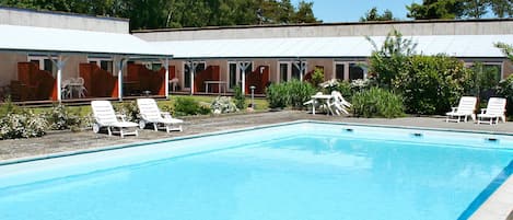 A swimming pool with lounge chairs and a covered outdoor area with tables and chairs.