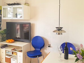 Een kamer met een televisie, een blauwe stoel, een fles wijn en een vaas met bloemen.