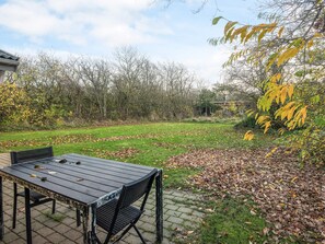 An outdoor patio area with a table and chairs, surrounded by a grassy lawn and trees. - Reposeful Holiday Home in Skjern near Sea (Skjern)