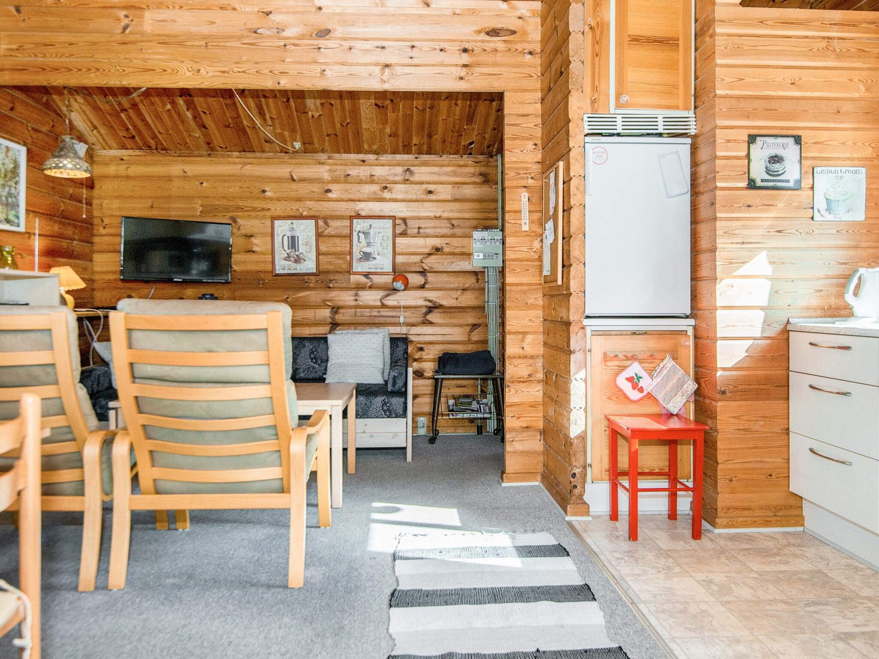 A cozy cabin interior with a wooden interior, a television, a small kitchen area, and a dining space with wooden chairs.