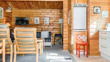 A cozy cabin interior with a wooden interior, a television, a small kitchen area, and a dining space with wooden chairs.
