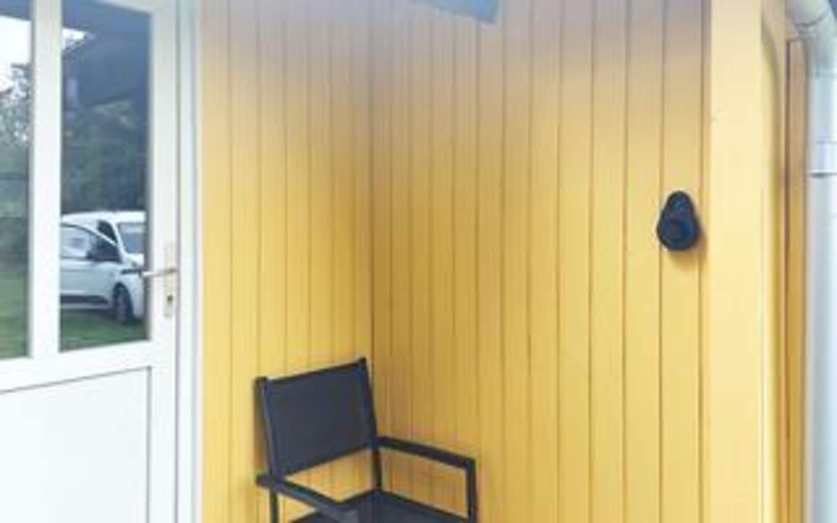 A room with a yellow wall, a black chair, and a small black object on the wall.
