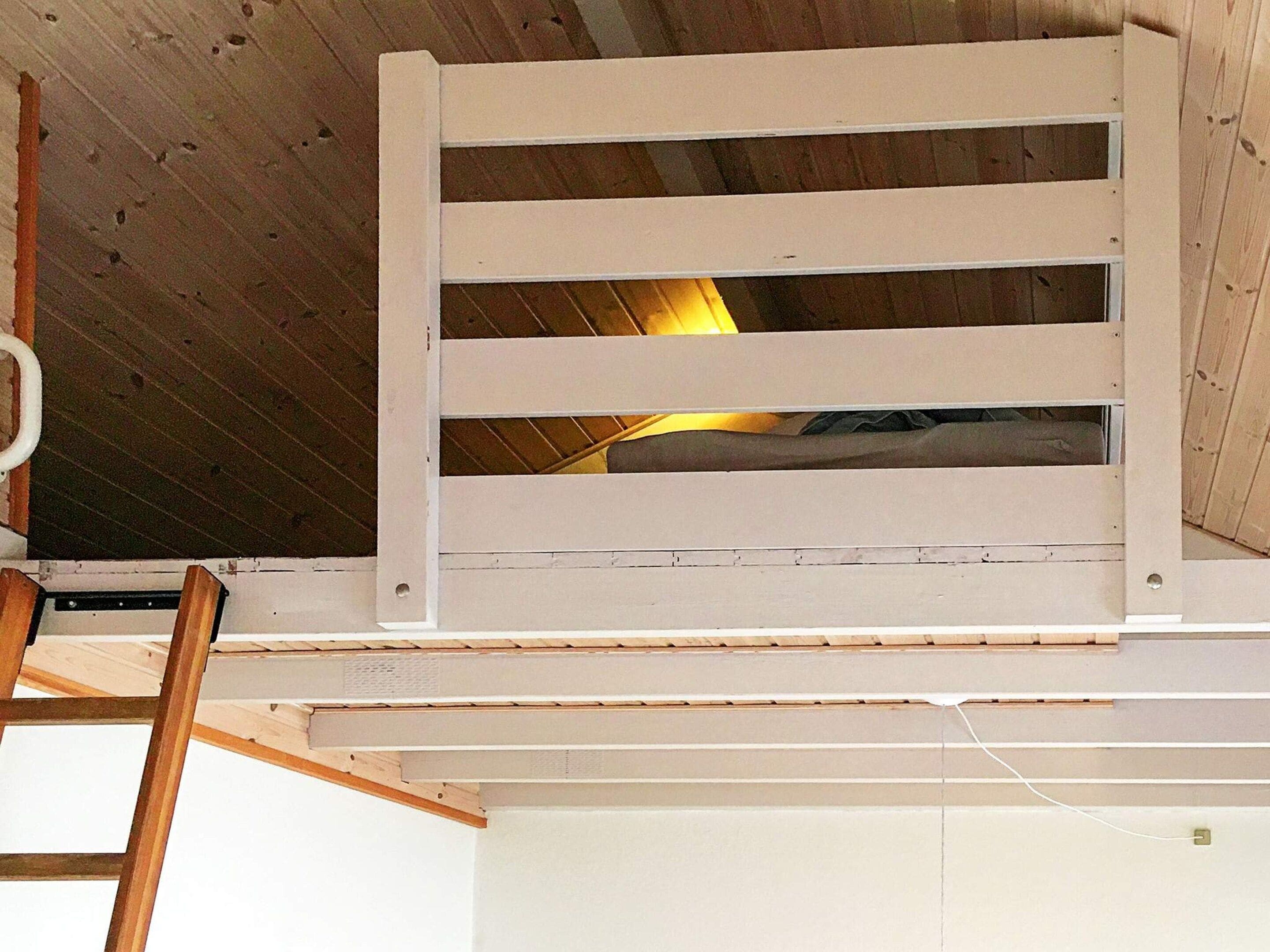 Une pièce avec un plafond en pente, un ventilateur de plafond blanc et une échelle en bois.