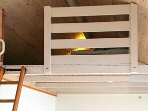 Ein Zimmer mit schrägem Dach, einem weißen Deckenventilator und einer Holzleiter.