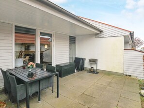 A patio with a table and chairs, a grill, and a sliding glass door leading to a covered area. - 4 Person Holiday Home in Aeroskobing (Aeroskobing)
