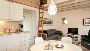 A modern kitchen with white cabinets, a coffee machine, and a sink. There is a dining area with a round table and chairs, and a living room with a sofa and a TV. - 4 Person Holiday Home in Aeroskobing (Aeroskobing)