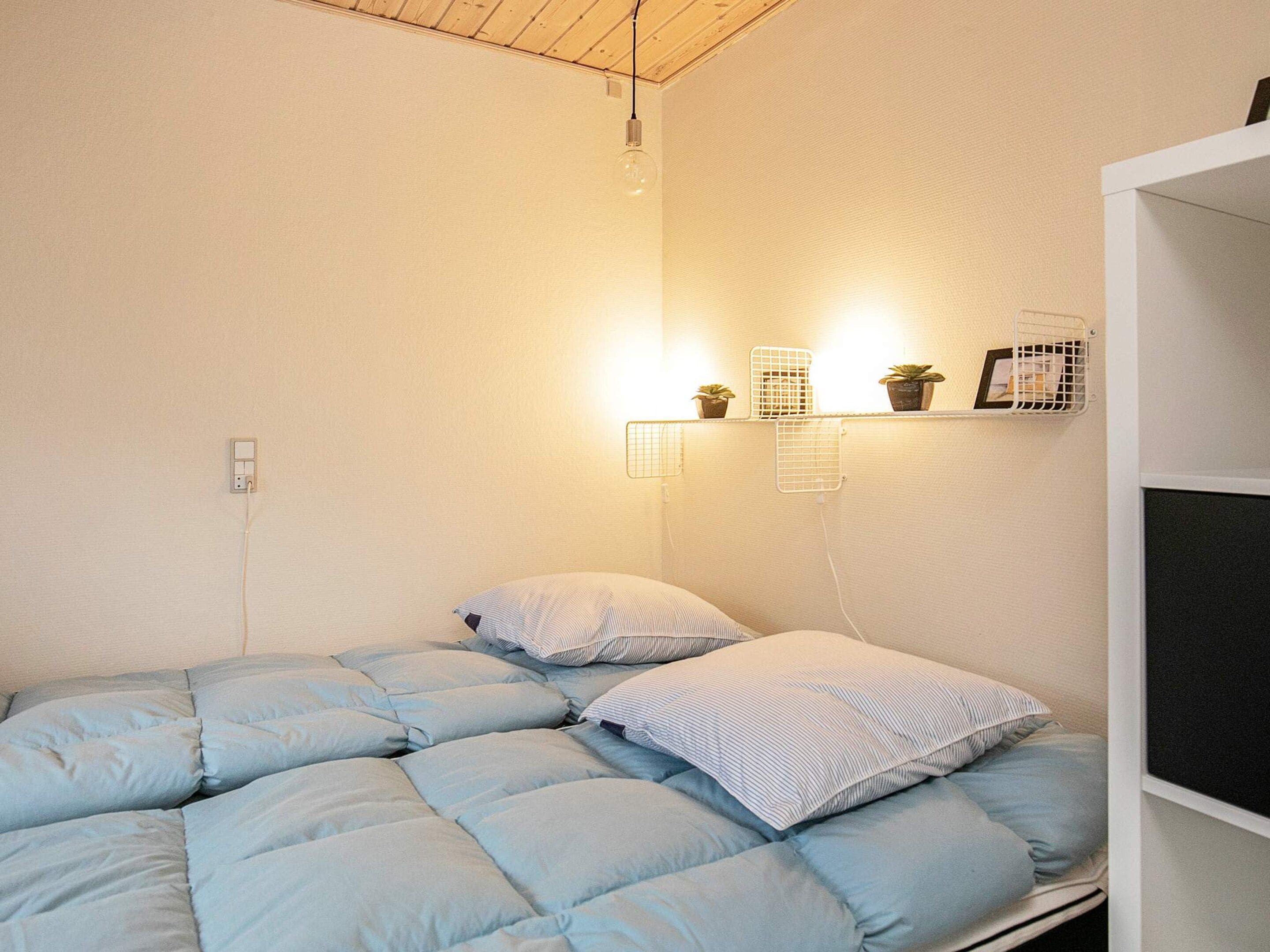 Une chambre avec un lit, une étagère fixée au mur avec des plantes et une prise de courant.