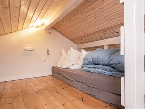 A small, cozy room with a sloped ceiling, wooden flooring, a bed with pillows, and a wall-mounted light fixture. - 4 Person Holiday Home in Aeroskobing (Aeroskobing)