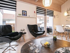 A modern living room with a round table, two black leather chairs, a glass coffee table, and a dining area with a white table and chairs.