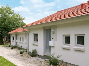 A white building with a red-tiled roof, multiple windows, and a small garden area with gravel and plants.