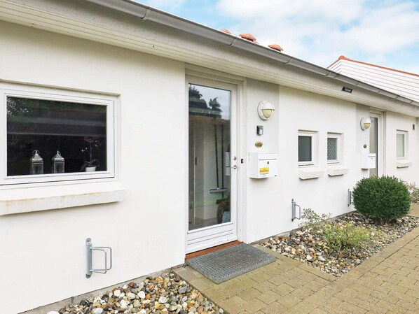 A white building with a door, windows, and a small garden area with pebbles and a bush. - 4 Person Holiday Home in Aeroskobing (Aeroskobing)