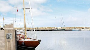 A wooden dock with a boat moored to it, a calm water body, and a rocky shoreline in the background. - 4 Person Holiday Home in Aeroskobing (Aeroskobing)
