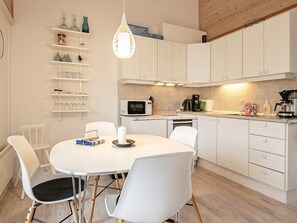 A modern kitchen with white cabinetry, a round dining table, and chairs. There are shelves with glassware and a hanging light fixture.