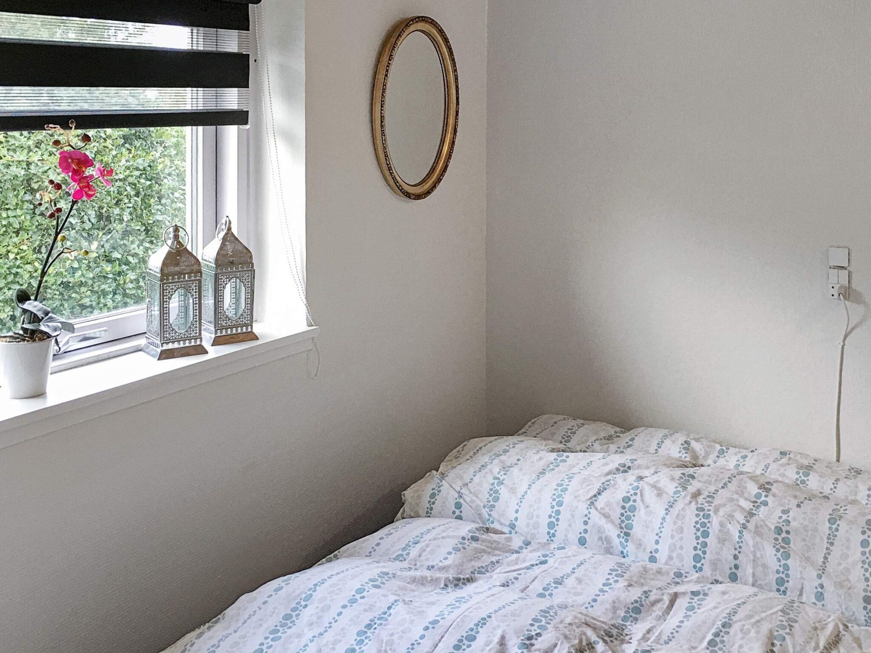 A bedroom with a bed, a window with a view of greenery, and decorative items on the windowsill.