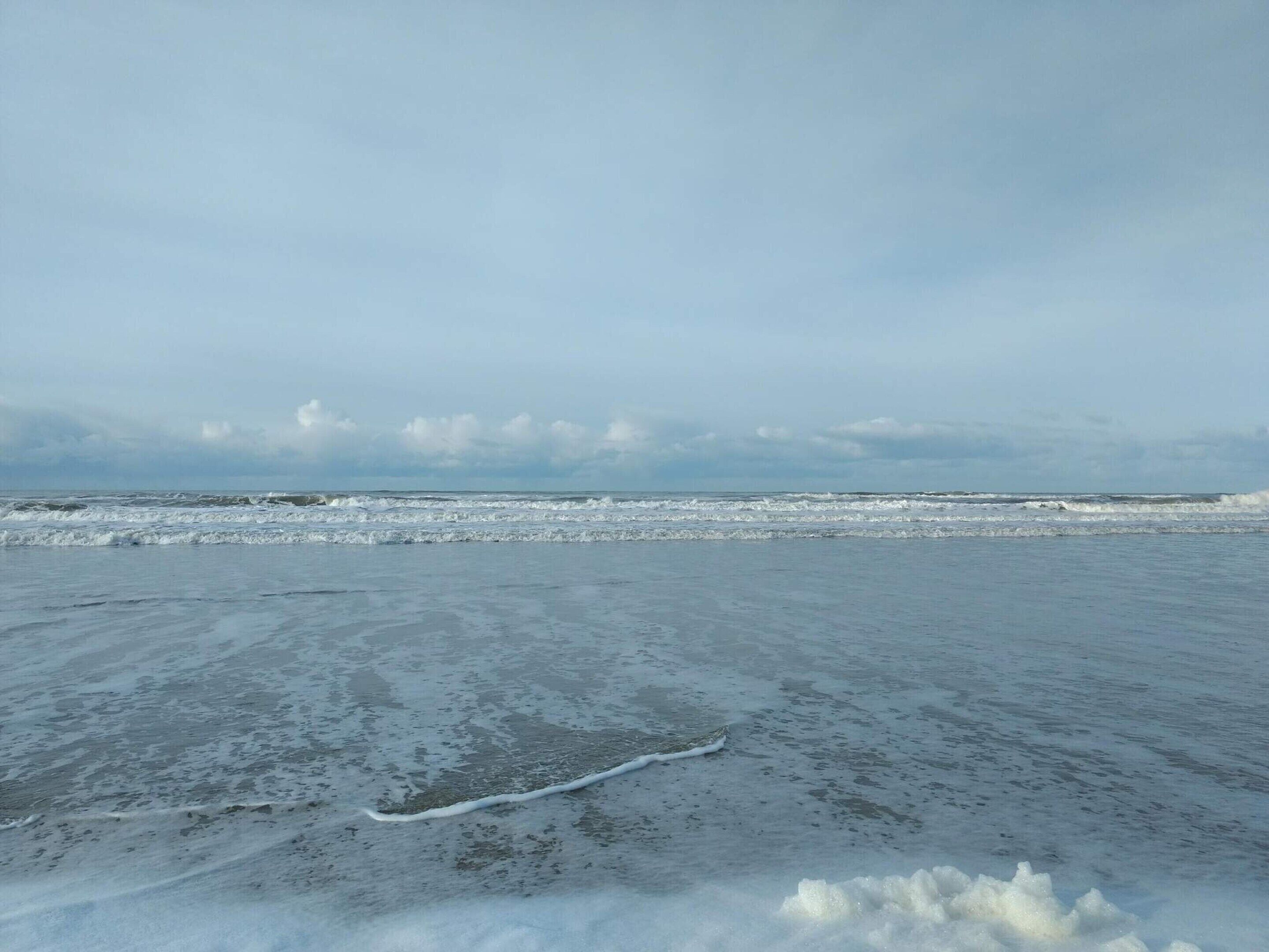 Een strand met een vlak, ijsachtig oppervlak en golven die de kust naderen.