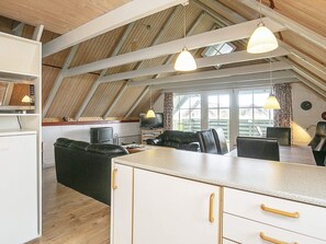 A loft-style living space with a sloped ceiling, a kitchenette, a dining area, and a seating area with a sofa and chairs.