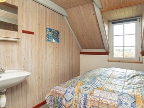 A bedroom with a wooden sloped ceiling, a window with a view, a bed with a patterned bedspread, and a white sink.