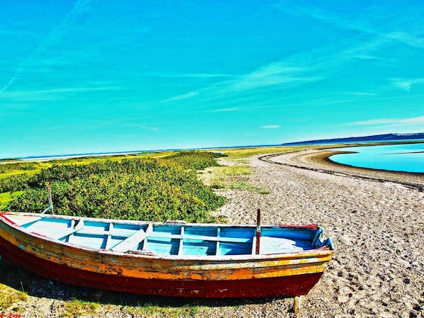 A boat on a pebbly shore with a lake and forest in the background.