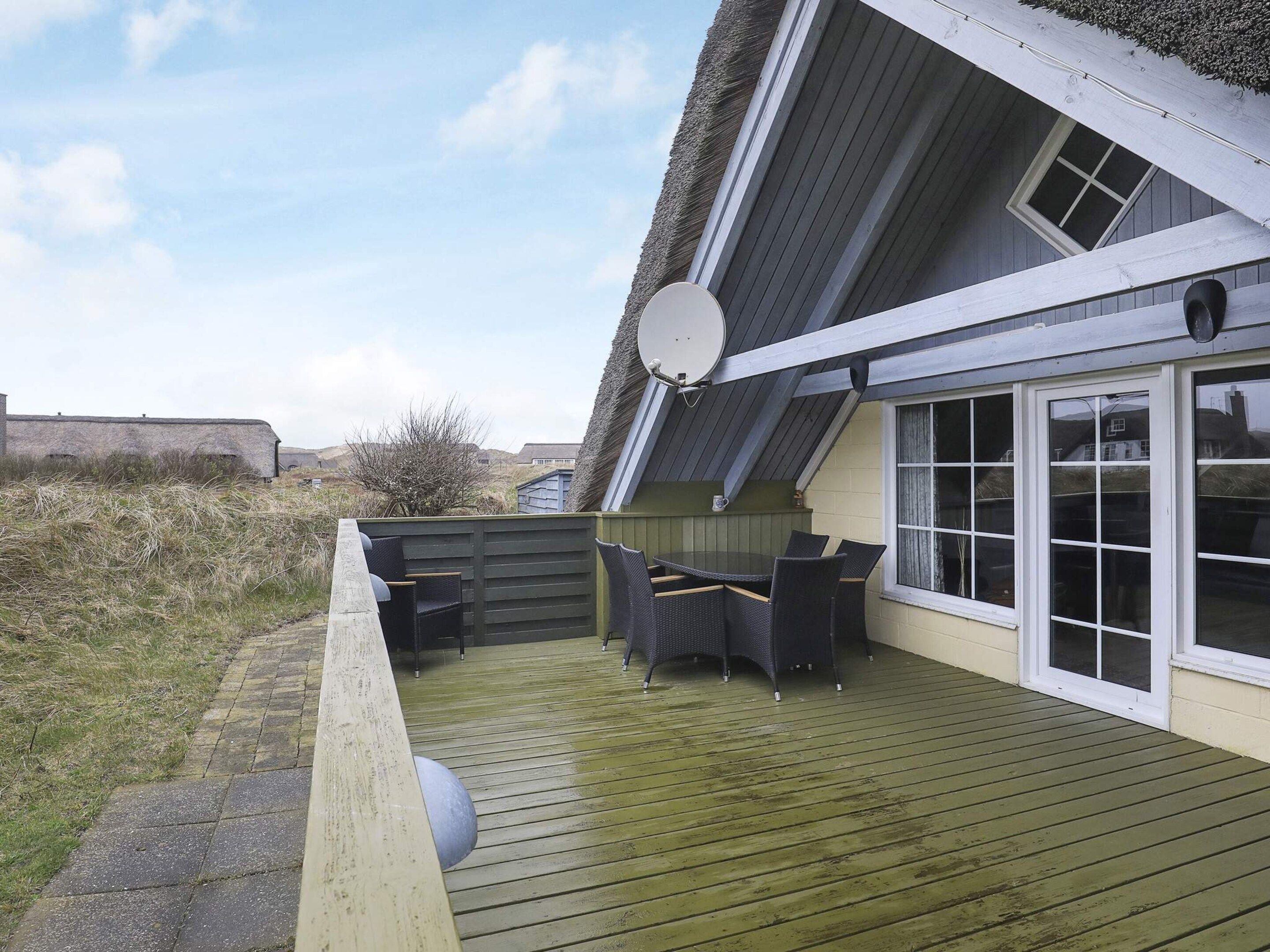 A covered outdoor area with a wooden deck, a table with chairs, and a satellite dish.