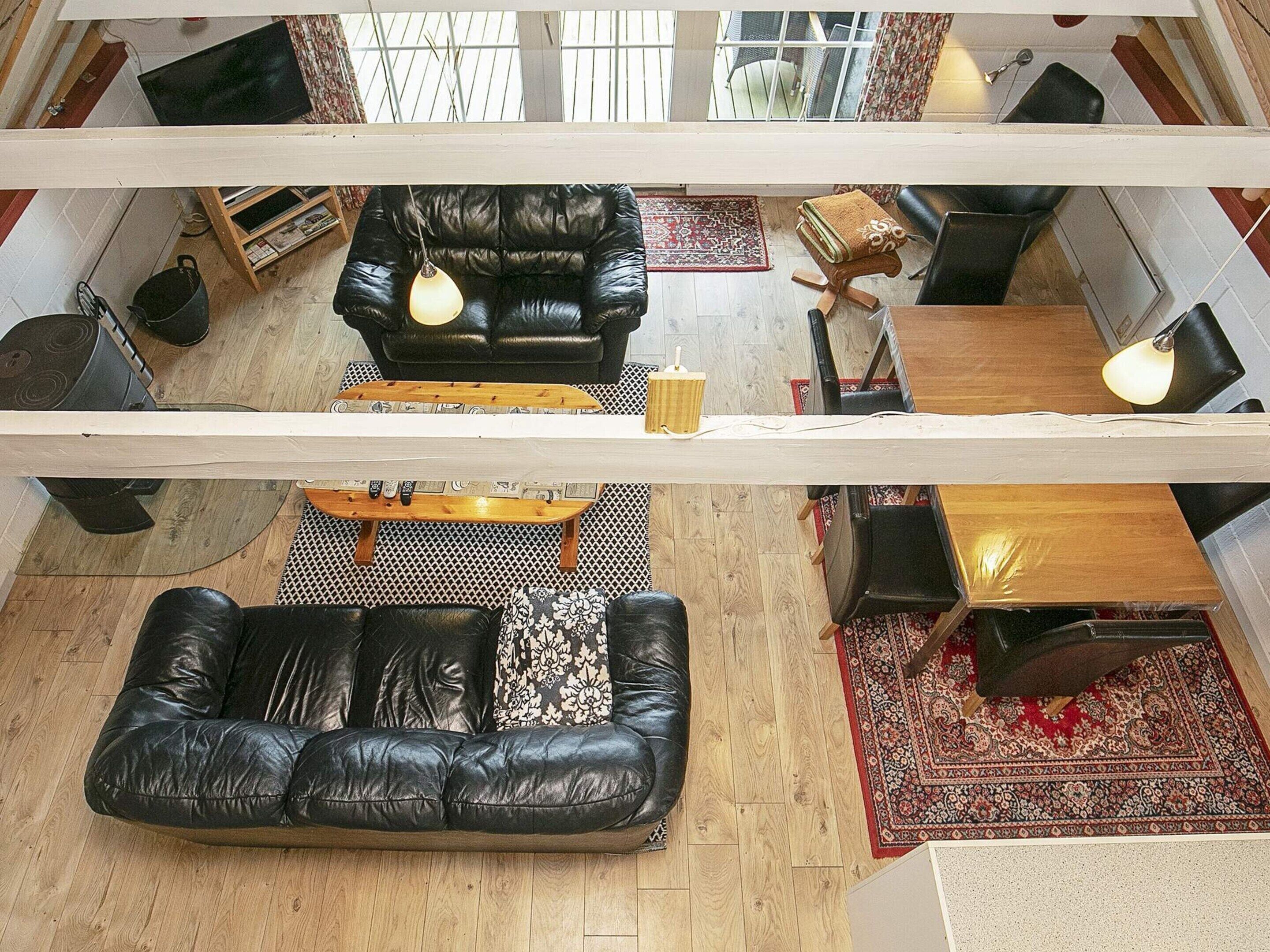 A high-ceilinged living room with a black leather sofa, a wooden coffee table, and a patterned rug.