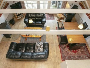 A high-ceilinged living room with a black leather sofa, a wooden coffee table, and a patterned rug.