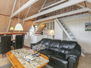 A loft-style room with a black leather sofa, wooden dining table, and a kitchen area with a staircase.