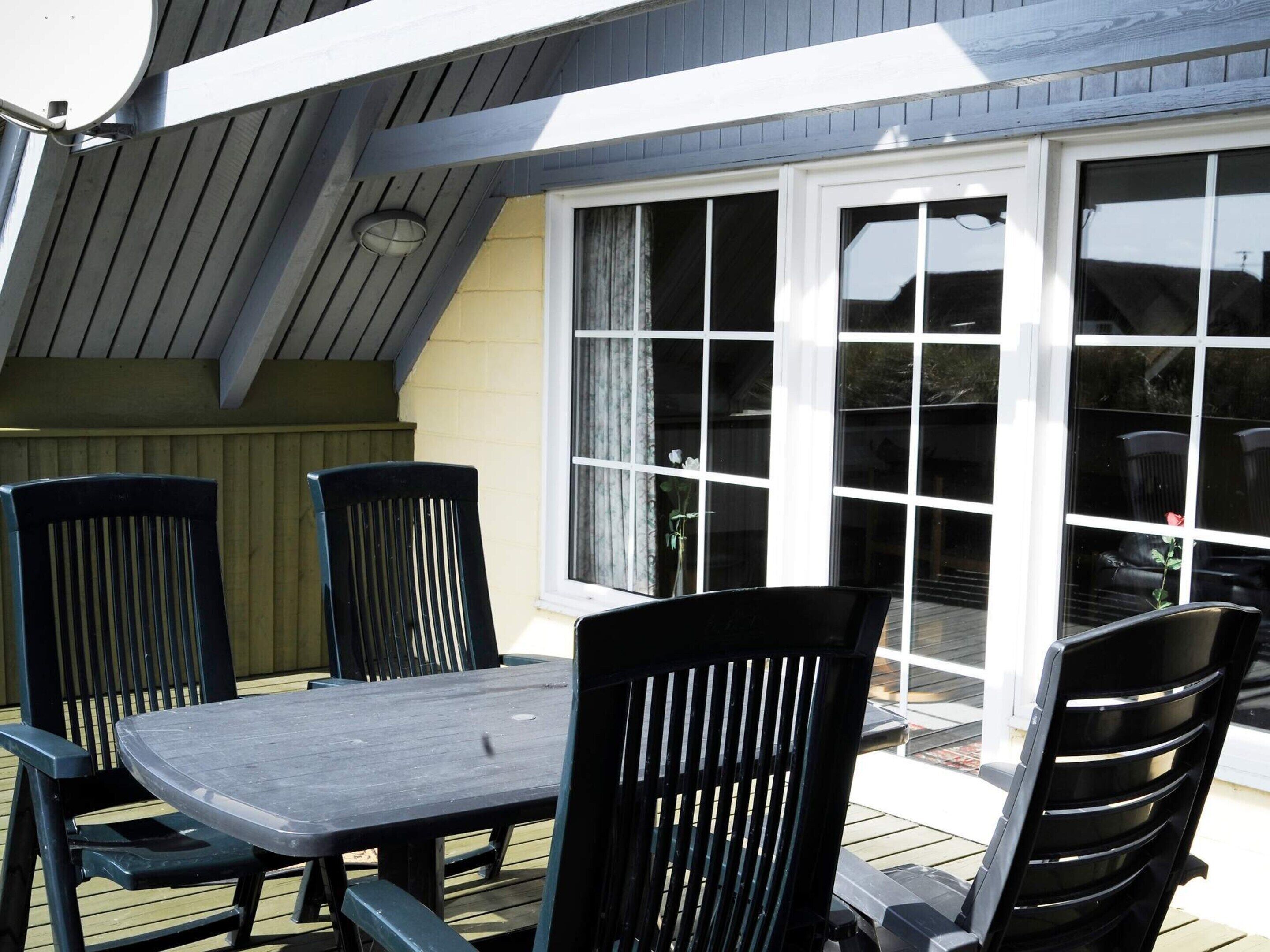 A patio with a table and chairs, a sliding glass door, and a wooden deck.