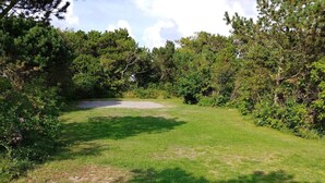 Une zone herbeuse avec de nombreux arbres et arbustes, un sentier de gravier et un ciel dégagé.